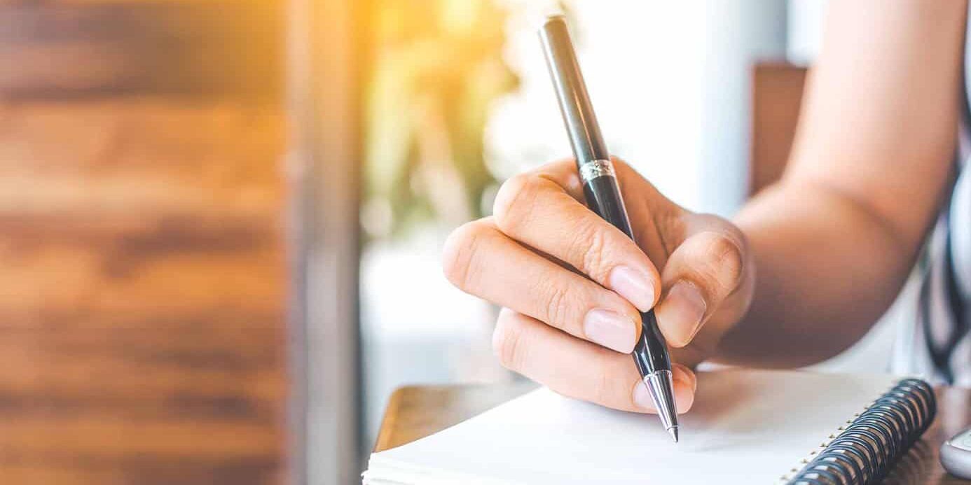 womans-hand-writing-in-notebook hand with pencil writing on a notebook