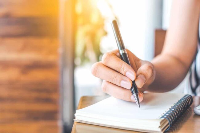womans-hand-writing-in-notebook hand with pencil writing on a notebook